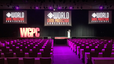 An empty meeting room with chairs lined up facing a stage with three large screens suspended from the ceiling.